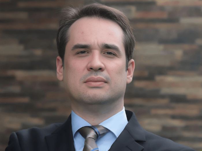 Retrato profissional de Filipe Augusto de Moura Meireles, advogado jovem, terno azul-marinho, sorriso confiante, fundo verde natural, iluminação suave ao ar livre, fotografia corporativa realista